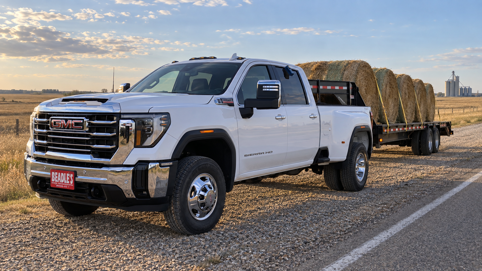 A Summit White 2026 GMC Sierra 3500 HD SLT dually pulling a gooseneck hay trailer on a two-lane shoulder near Mobridge, South Dakota