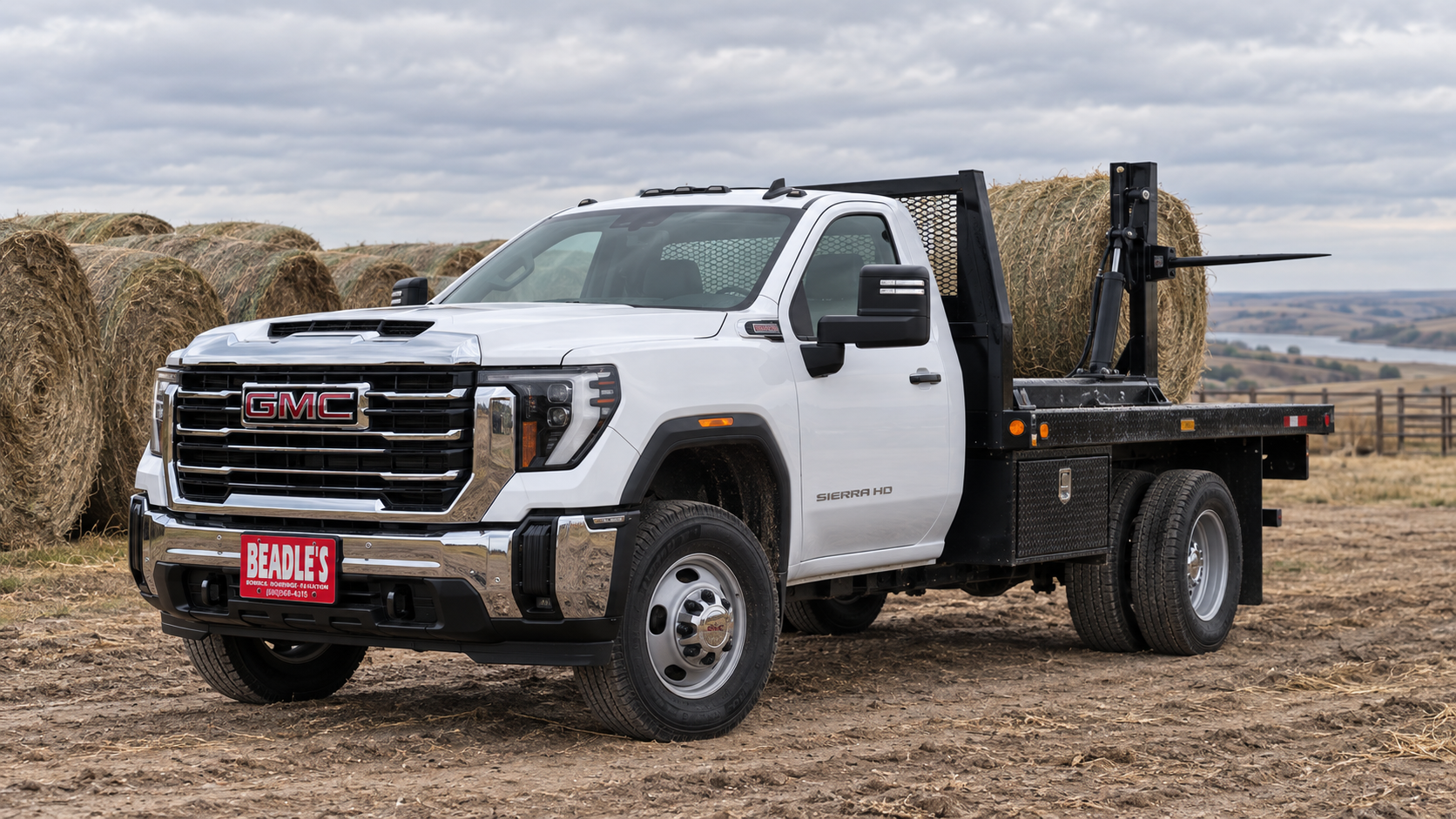 Summit White 2027 GMC Sierra 3500 HD chassis cab dually carrying a flatbed bale bed in a hay yard near Mobridge, South Dakota